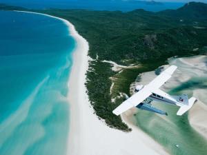 an airplane flying over a beach and the ocean at Mango Sands Villa in Airlie Beach