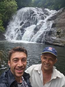two men standing in front of a waterfall at Rainforest View in Deniyaya