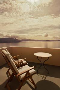 einen Stuhl und einen Tisch auf einem Balkon mit Blick auf das Wasser in der Unterkunft THE A COLLECTION by K&K in Oia