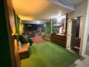 博瓦利Sk inn hotel的一个男人坐在铺着绿色地毯的房间的长椅上