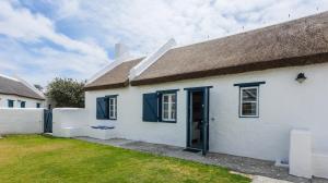 ein weißes Haus mit Strohdach und einem Garten in der Unterkunft Zandtorini Seaside Cottage in Struisbaai