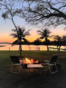 Deux chaises et un foyer dans un champ au coucher du soleil dans l'établissement Casa de Campo em frente ao Lago em Americana-SP, à Americana