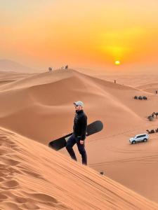 a man walking on a sand dune with a snowboard at Celestial luxury Camp in Merzouga