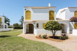 ein weißes Haus mit gelben Fensterläden und ein Baum in der Unterkunft Aldeia do Golfe - Private condominium by HD in Estibeira
