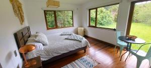 ein Schlafzimmer mit einem Bett und einem Tisch und zwei Fenstern in der Unterkunft Anahata Lodge, Alojamiento Tranquilo en Medio de la Naturaleza in Puerto Varas + 10 Fotos
