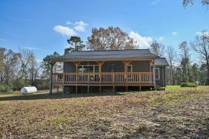 a large house with a large deck on a field at Three Oaks in Mena