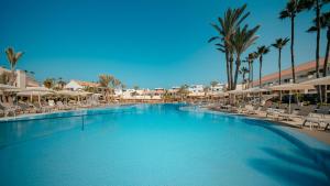 ein großer Swimmingpool mit Stühlen und Palmen in der Unterkunft HD Lobos Natura Fuerteventura in Corralejo