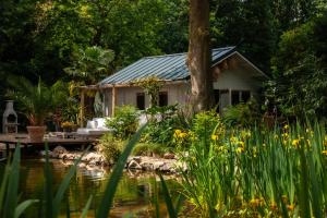 ein Haus in einem Garten mit einem Teich und Blumen in der Unterkunft CoCo Cabin Luxe Tiny House - Privé Hottub - Strand & zwemvijver - Privacy in Woudenberg