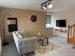 ein Wohnzimmer mit einer Couch, einem Tisch und einem Fernseher in der Unterkunft Maison aux pieds du circuit de Mirecourt in Baudricourt