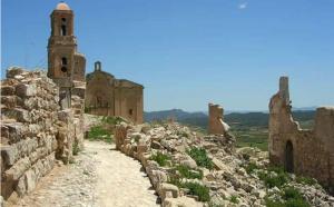un muro di pietra con un edificio e una torre dell'orologio di Lo Pateret a Corbera