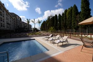 ドミンゴス・マルチンスにあるApart Vista Azul - Conforto com a vista para a mata de pinheirosの建物の隣に椅子とパラソルのあるプール