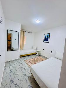 une chambre blanche avec deux lits et un miroir dans l'établissement Maison N 20, à Oulad Akkou