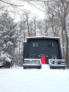 une maison noire avec une porte rouge dans la neige dans l'établissement Modern chalet for 8 people with Fireplace, Hot Tub and nearby Skiing, à Tobyhanna