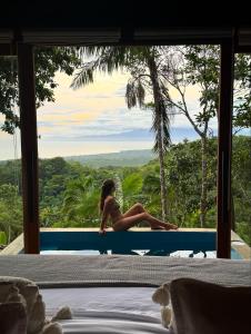 eine Frau sitzt auf einem Bett in einem Zimmer mit Aussicht in der Unterkunft Drako Villas- Adults only in Siquijor