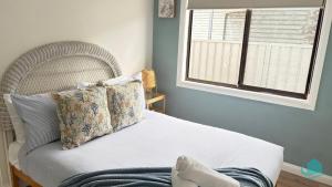 ein Bett mit Kissen und ein Fenster in einem Schlafzimmer in der Unterkunft Barefoot at Blacksmiths Beach in Blacksmiths