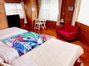 une chambre avec deux lits et une chaise rouge dans l'établissement ゲストハウス奄美ルリカケス, à Amami