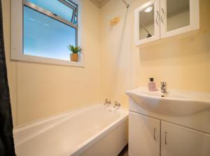 ein Bad mit einem Waschbecken, einer Badewanne und einem Fenster in der Unterkunft Te Anau Holiday House in Te Anau