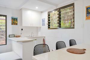 a kitchen with white cabinets and a table and chairs at Edge Hill Apartment under Queenslander w Pool in Edge Hill