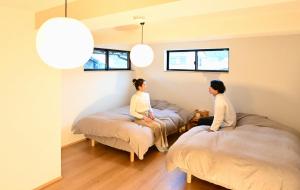 Zwei Frauen sitzen auf Betten in einem Zimmer mit Fenstern in der Unterkunft 御宿Fuku in Kannoura