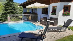 une piscine avec des chaises et un parasol à côté d'une maison dans l'établissement Ferienwohnung Wiesengrund In Bayerisch Eisenstein, à Bayerisch Eisenstein