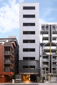 a tall white building next to two tall buildings at ALPHABED INN Hakata station front in Fukuoka