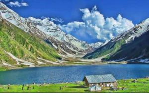 a barn in a field next to a mountain lake at Rozhok Hotel in Dargai