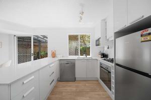 Acacia - Mount Coolum 3BD Townhouse في Yaroomba: مطبخ بخزائن بيضاء وثلاجة من الفولاذ المقاوم للصدأ