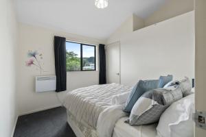 a white bedroom with a bed and a window at Atarau Grove Holiday House in Paraparaumu