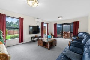 a living room with a couch and a tv at Atarau Grove Holiday House in Paraparaumu