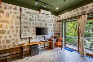 a room with a stone wall with a desk and a tv at Granny's Den BY ELIVAAS in Dhanaulti