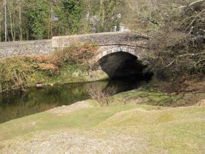 un puente de piedra sobre un río en un bosque en Magpie's Rest, en Horrabridge 1 foto más