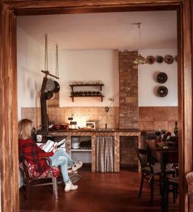 a woman sitting in a chair reading a book in a kitchen at Halháza vendégház in Sirok