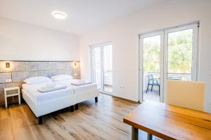 a white bedroom with a bed and a table at Resort Trcol in Novalja