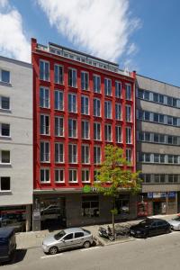 ein rotes Gebäude mit Autos auf einem Parkplatz in der Unterkunft H+ Hotel München in München