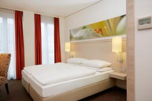 a white bedroom with a bed and a chair at H+ Hotel München in Munich