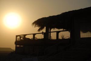 Ein Gebäude mit Strohdach, im Hintergrund die Sonne in der Unterkunft חאן השיירות- אוהלים בדואיים וקמפינג in Midreshet Ben Gurion