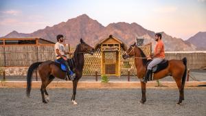 Dos personas montando a caballo frente a un edificio. en Subla Camp, en Hatta