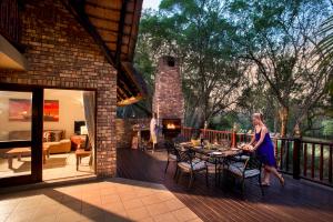 una mujer de pie en una cubierta con una mesa en Kruger Park Lodge, en Hazyview