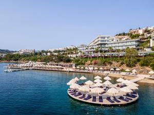 京多安Cape Bodrum Luxury Hotel & Beach的水面上摆放着一组沙滩椅和遮阳伞