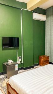 ein Schlafzimmer mit einer grünen Wand mit einem Bett und einem Fernseher in der Unterkunft Wyne's Hotel in Mbale