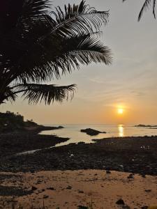 una puesta de sol en una playa con una palmera en Colomb Beach Huts, en Patnem