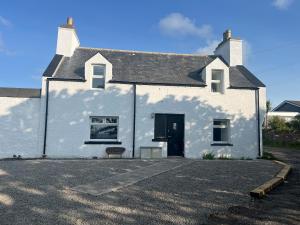 a white building with a door and a bench in front at Highland Park Cottage in Kirkwall