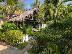 a house with a thatched roof and palm trees at Garner house watamu in Watamu