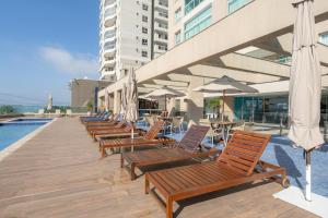 a row of wooden chairs and umbrellas next to a pool at Apartamento em condomínio HOME CLUB, cozinha completa, PISCINA e JACUZZI aquecida, SAUNA, ACADEMIA, quadra de esportes playground infantil, salão de jogos a 40m da PRAIA e 15min do Beto Carreiro in Piçarras