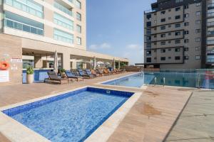 a swimming pool with lounge chairs next to a building at Apartamento em condomínio HOME CLUB, cozinha completa, PISCINA e JACUZZI aquecida, SAUNA, ACADEMIA, quadra de esportes playground infantil, salão de jogos a 40m da PRAIA e 15min do Beto Carreiro in Piçarras