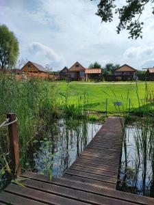 un pont en bois enjambant un étang avec des maisons en arrière-plan dans l'établissement Siedlisko nr 5A nad jeziorem Skarlińskim, jezioro, mazury, domki letniskowe, bania, à Kurzętnik