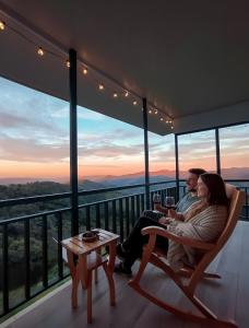 un hombre y una mujer sentados en un balcón con una copa de vino en Nosara Hideaway 3 - BREAKFAST INCLUDED & Mountain View Cabins, en Nosara