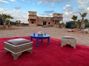 Ein Tisch und zwei Hocker auf einem roten Teppich mit einem Haus in der Unterkunft AISHAMA Healing House in Aït Ourir
