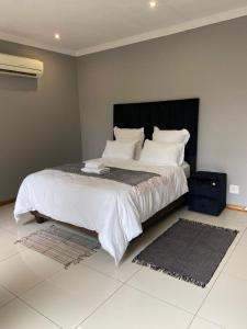 una habitación con una cama grande con sábanas y almohadas blancas en Hazel Nest Ezulwini, en Ezulwini