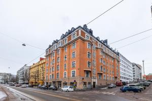a large brick building on a street with parked cars at Bright Loft Apartment Steps From Linnanmäki & Alppipuisto in Helsinki